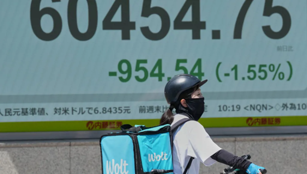 A delivery person on a bicycle waits for a traffic light near an electronic stock board showing Japan's Nikkei index at a securities firm Monday, May 18, 2026, in Tokyo. (AP Photo/Eugene Hoshiko)