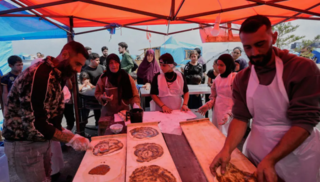 Soubhiye Zeiter, 63, centre left, a displaced woman who fled her home with her family in Beirut's southern suburbs, prepares with other workers mana'eesh, a popular Lebanese flatbread breakfast topped with thyme, to be distributed for displaced people at a small bakery in a tented settlement along Beirut's waterfront, Lebanon, Thursday, May 21, 2026. (AP Photo/Hussein Malla)