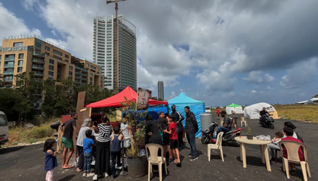 Displaced people who fled their homes due to the war between Israel and Hezbollah, gather outside a small bakery to receive mana'eesh, a popular Lebanese flatbread breakfast topped with thyme, in a tented settlement along Beirut's waterfront, Lebanon, Thursday, May 21, 2026. (AP Photo/Hussein Malla)