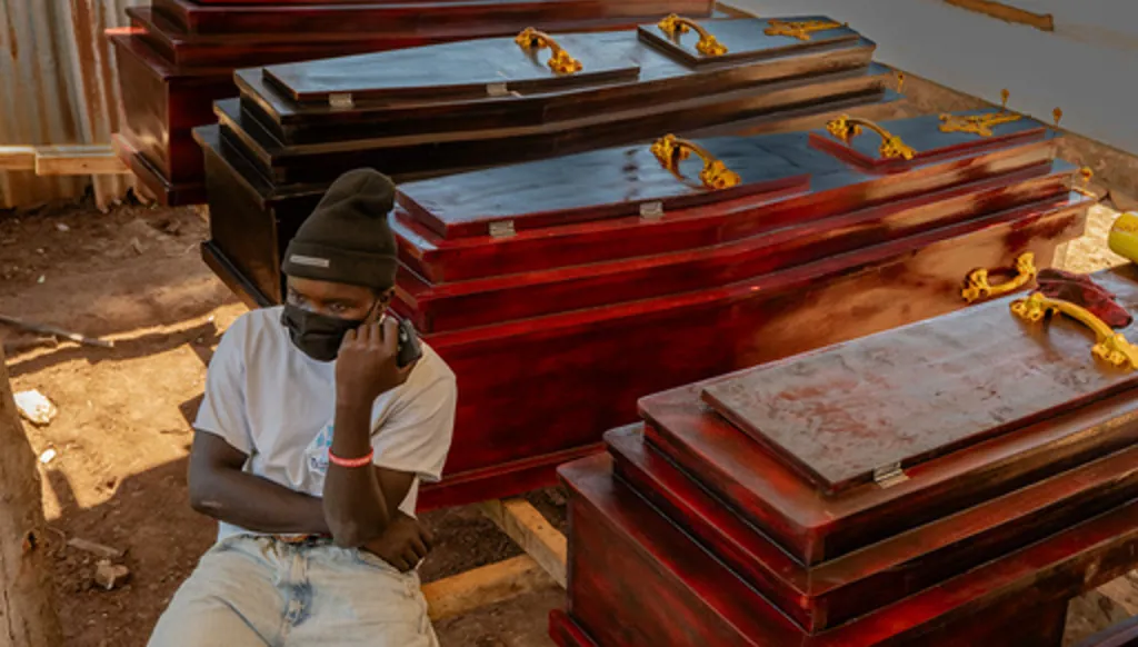 Djakisa Christian, 18, a funeral home manager, sits in front of coffins for sale at his shop in Bunia, Congo, Friday, May 22, 2026. (AP Photo/Moses Sawasawa)