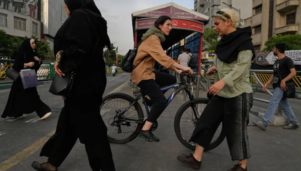 A woman rides a bicycle as others cross a street in downtown Tehran, Iran, Sunday, May 24, 2026. (AP Photo/Vahid Salemi)