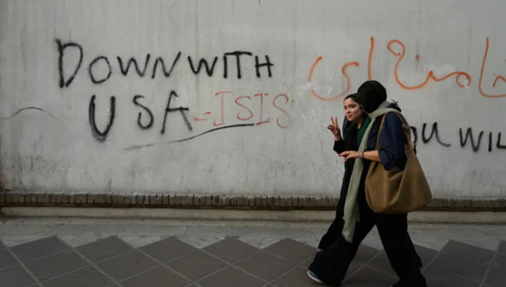 A woman reacts to the camera as she walks past an anti-U.S. graffiti painted on the wall of the British Embassy in Tehran, Iran, Saturday, June 6, 2026. (AP Photo/Vahid Salemi)