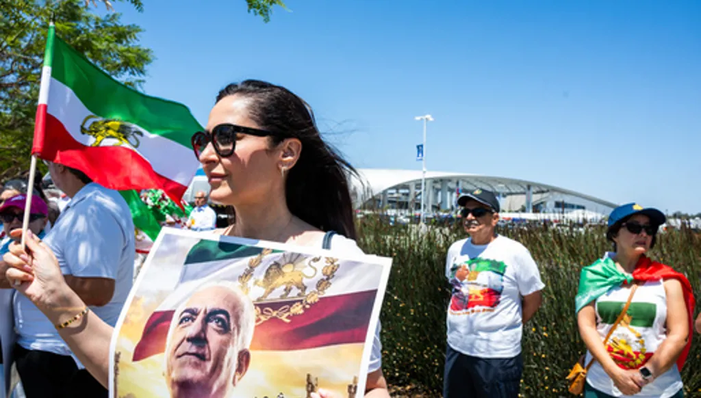 A woman holds a flag and poster during a protest in reaction to FIFA's ban of Iran's pre-revolutionary flag inside World Cup stadiums Sunday, June 7, 2026, in Inglewood, Calif. (AP Photo/Benjamin Hanson)