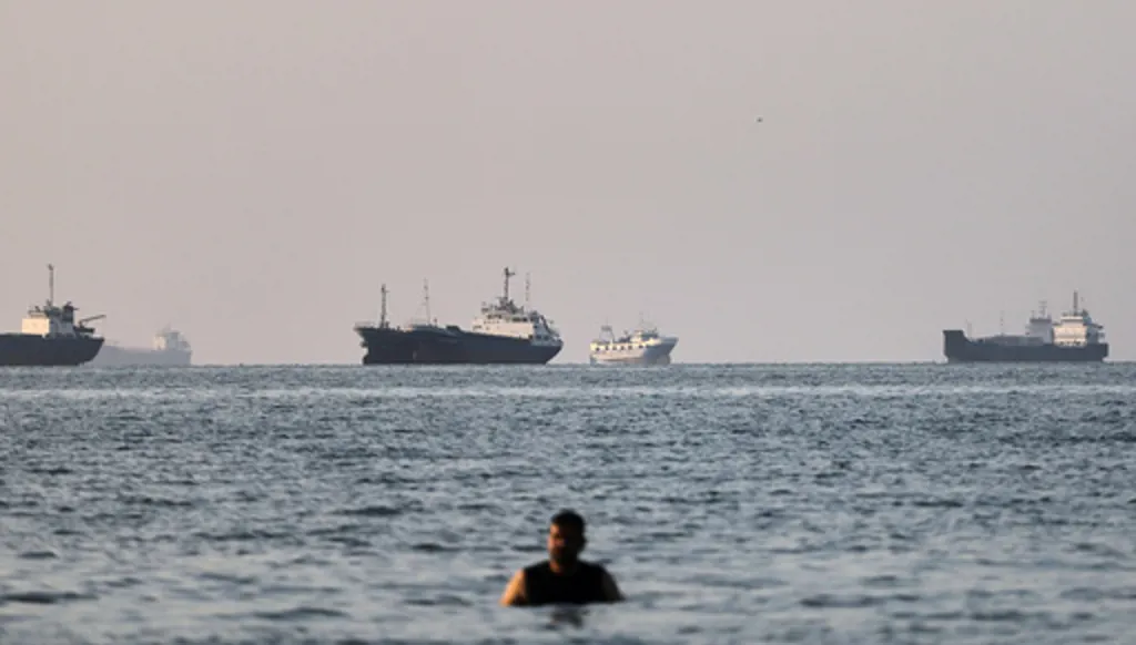 A person stands on shallow water as cargo and commercial vessels are anchored in the Strait of Hormuz off Bandar Abbas, Iran, Monday, June 8, 2026. (Amirhosein Khorgooi/ISNA via AP)