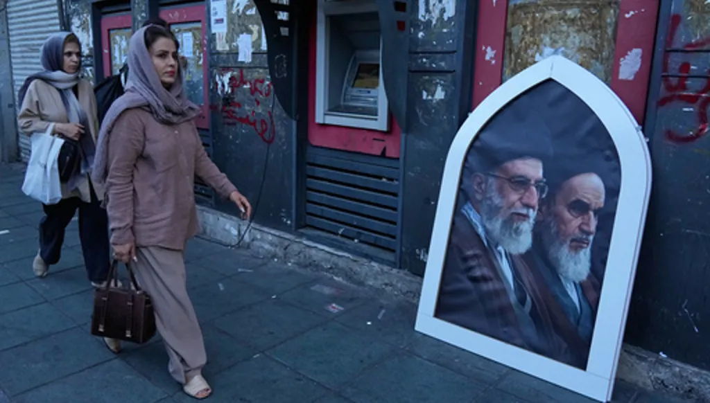 Pedestrians walk past a poster showing the slain Iranian Supreme Leader Ayatollah Ali Khamenei, left, and the late revolutionary founder Ayatollah Khomeini on a sidewalk at the Islamic Revolution square in Tehran, Iran, Sunday, June 14, 2026. (AP Photo/Vahid Salemi)