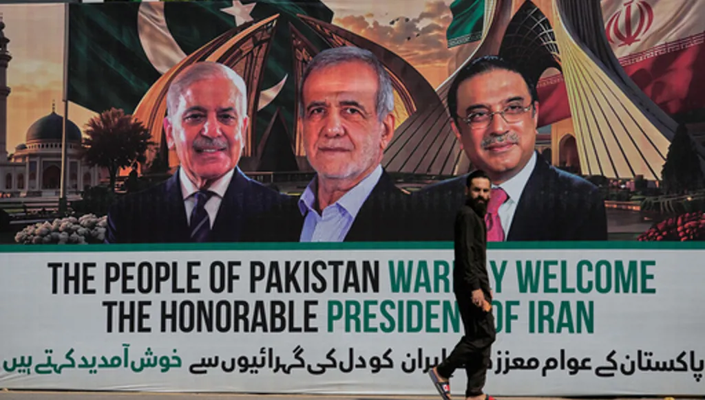 A man walks past a welcoming billboard featuring Iranian President Masoud Pezeshkian, center, with Pakistan President Asif Ali Zardari, right, and Shehbaz Sharif along a roadside in Islamabad, Pakistan, Tuesday, June 23, 2026. (AP Photo/Anjum Naveed)