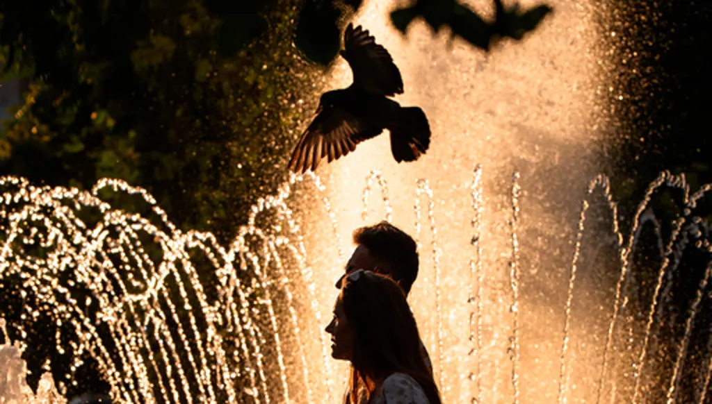 A couple walks by a public fountain on a torrid day, as the National Weather forecaster issued an extreme heat code red warning for parts of the country, in the coming days in Bucharest, Romania, Saturday, June 27, 2026. (AP Photo/Andreea Alexandru)