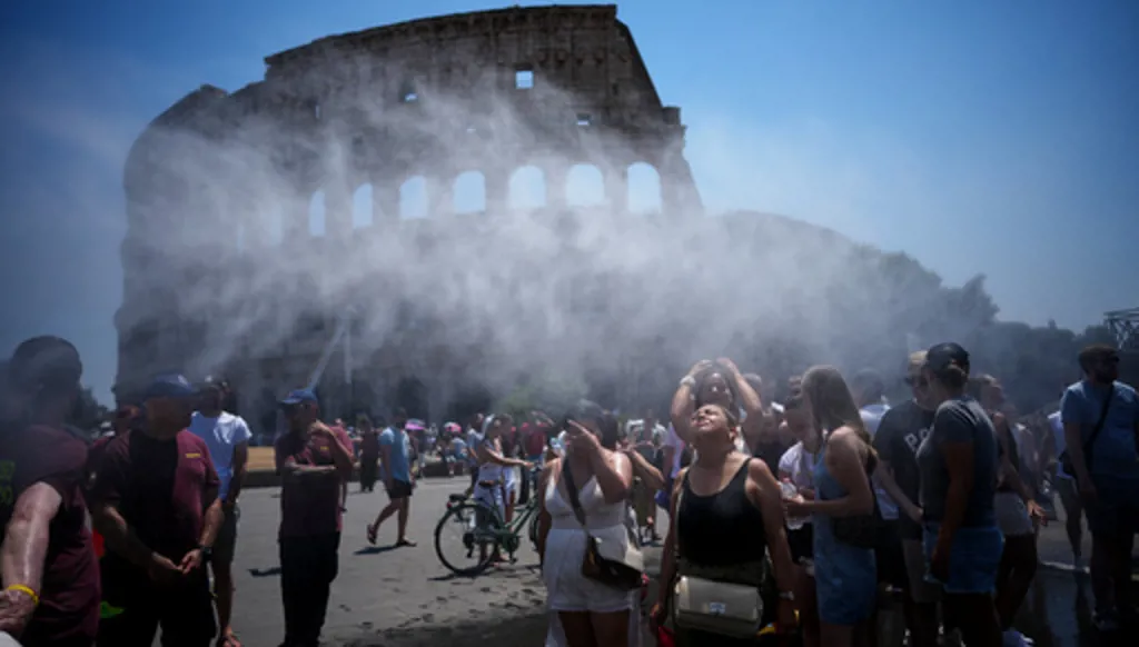 People refresh in front of a water-sprinkling cannon brought by Rome's municipality to relieve tourists visiting the Colosseum and Roman Forum as temperatures reach record highs, in Rome, Friday, June 26, 2026. (AP Photo/Andrew Medichini)
