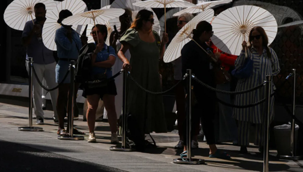 People use parasols to protect themselves from the sun as they queue outside a shop in London, Friday, June 26, 2026. (AP Photo/Kirsty Wigglesworth)