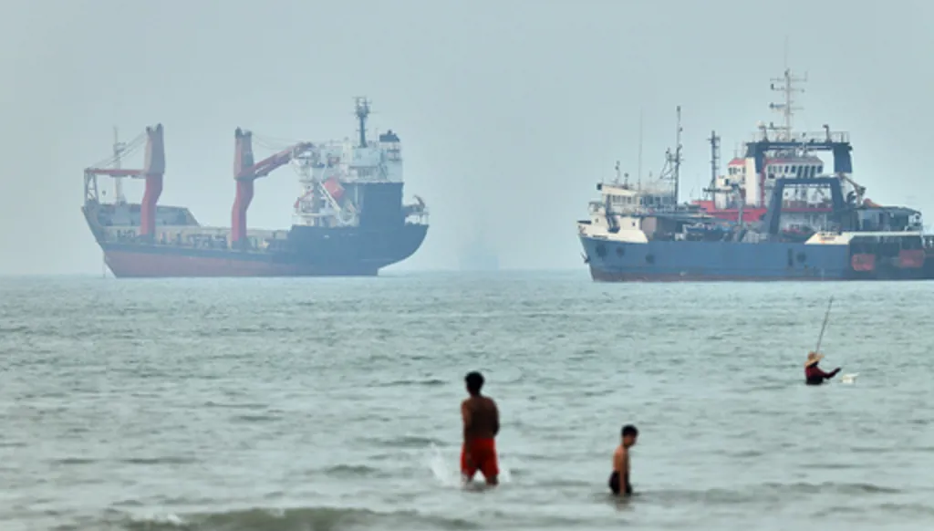 Children wade in the water with cargo ships at anchor in the background and a fisherman nearby, in the Strait of Hormuz off Bandar Abbas, Iran, Tuesday, June 30, 2026. (Amirhosein Khorgooi/ISNA via AP)