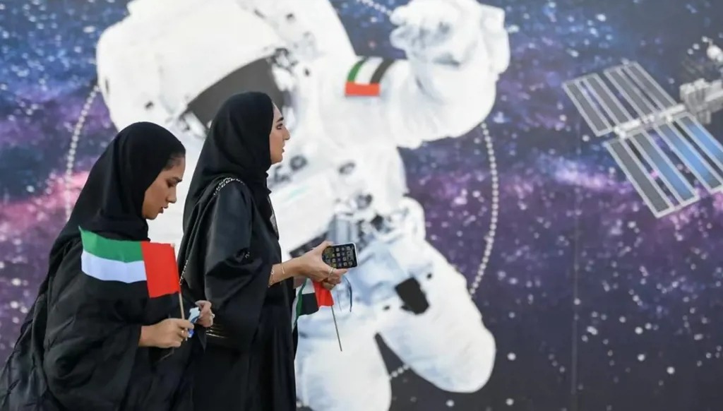 إماراتيتان تمران أمام رسم جداري يصور رائد فضاء يحمل العلم الإماراتي خارج مركز محمد بن راشد للفضاء. (أ ف ب)