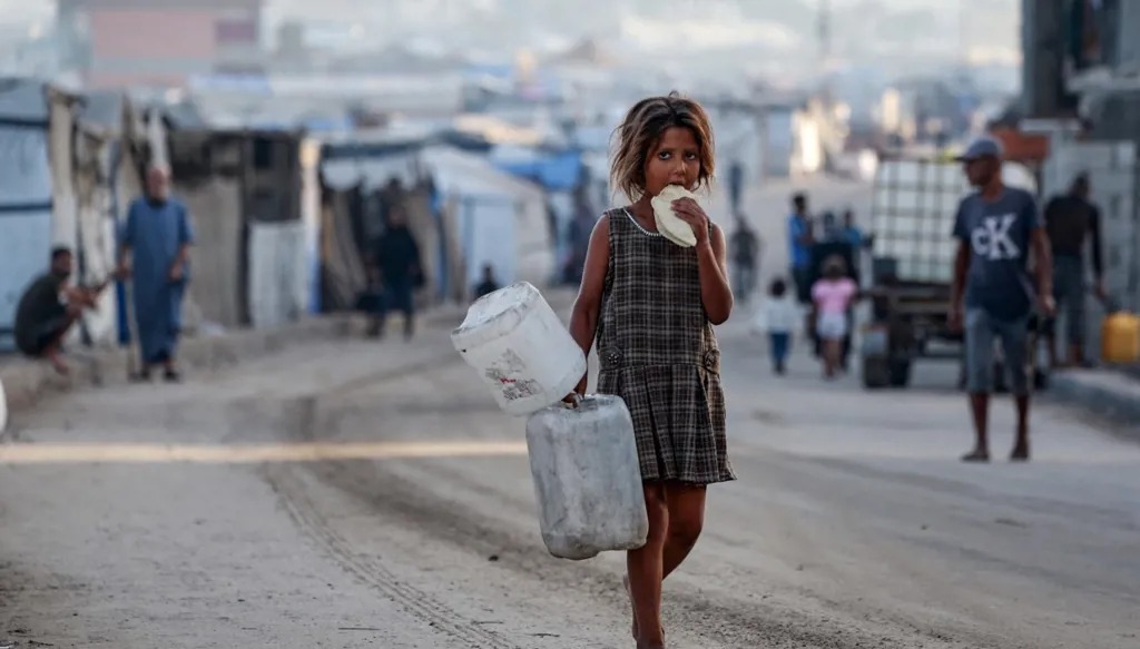 فتاة فلسطينية نازحة تأكل الخبز وهي تمشي حافية القدمين في أحد شوارع دير البلح وسط قطاع غزة. (أ ف ب)