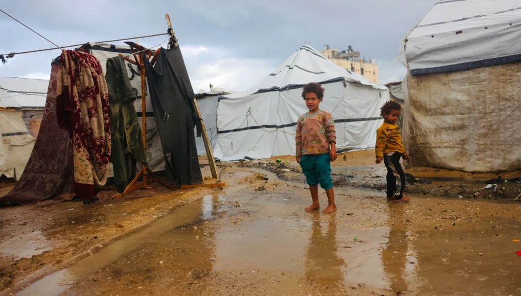 أولاد فلسطينيون يقفون أمام خميهم في دير البلح.(أف ب)