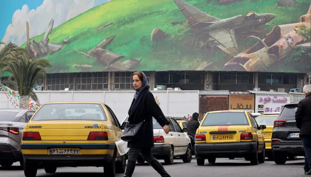 سيدة إيرانية تمر أمام لوحة إعلانية ضخمة مناهضة للولايات المتحدة في ساحة ولي عصر بطهران. (أ ف ب)