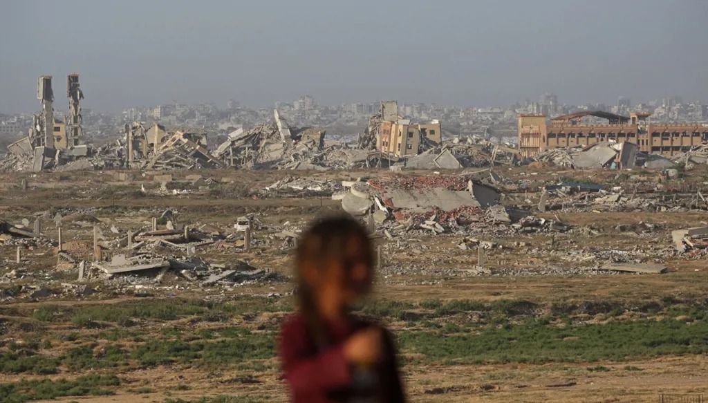 فتاة فلسطينية تقف أمام خلفية من المباني المدمرة في دير البلح، وسط قطاع غزة. (أ ف ب)
