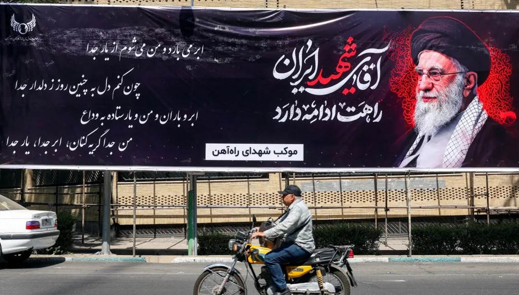 رجل يستقل دراجة نارية أمام صورة كبيرة للمرشد الإيراني الراحل علي خامنئي. (أ ف ب)