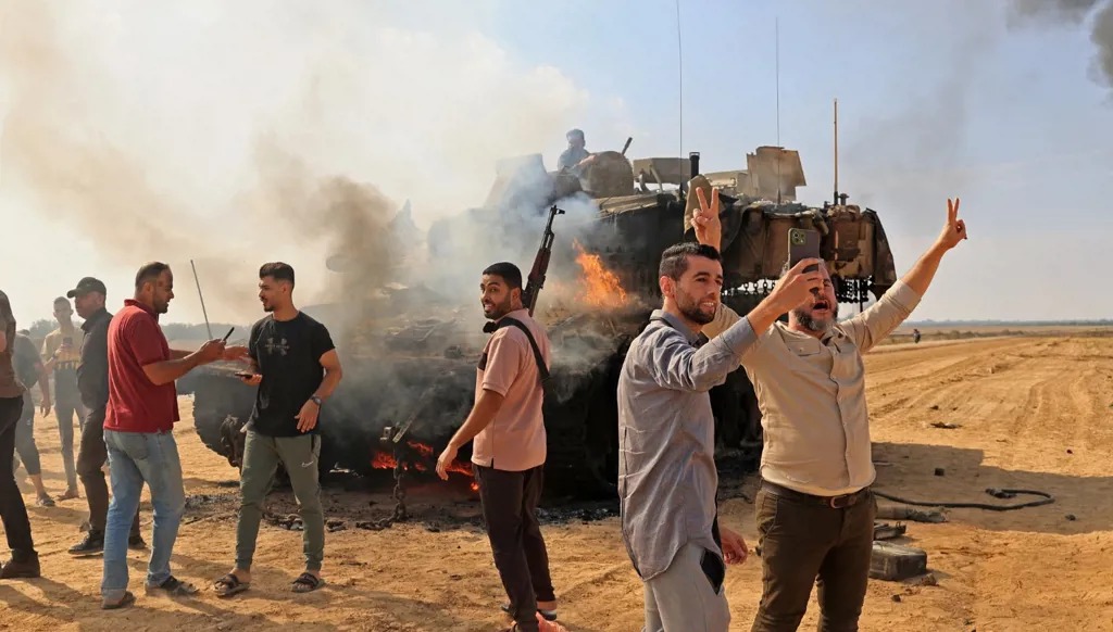 مسلحون فلسطينيون يتجمعون حول دبابة ميركافا إسرائيلية مشتعلة قرب السياج الحدودي بعد عبورهم من خان يونس في جنوب قطاع غزة، 7 تشرين الأول/أكتوبر 2023. (أ ف ب)
