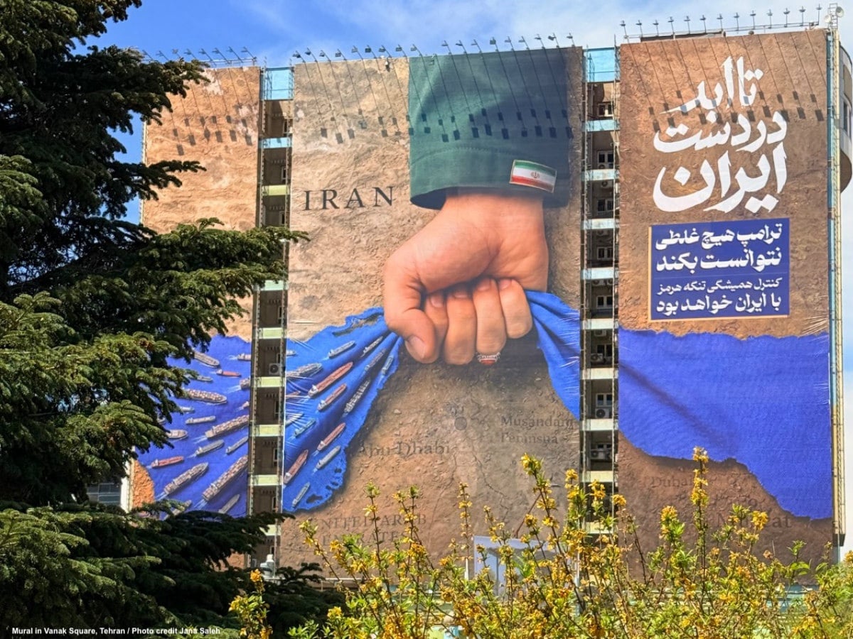 لوحة جدارية ضخمة في ساحة ونك بطهران تُظهر قبضة تحمل شارة العلم الإيراني فوق خريطة مضيق هرمز، مع سفن في مياهه.