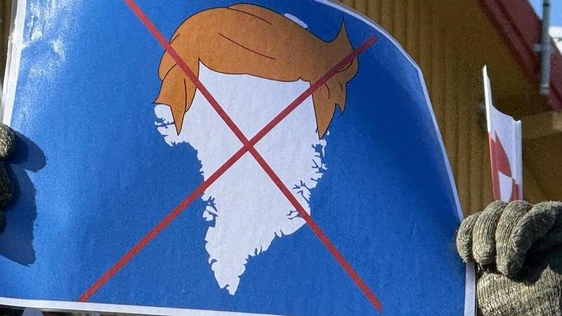 أحد المتظاهرين يرفع لافتة تحمل صورة لتسريحة شعر ترامب فوق خريطة غرينلاند، خلال احتجاج قرب مبنى القنصلية الأميركية خارج مدينة نوك في غرينلاند. (وكالات)