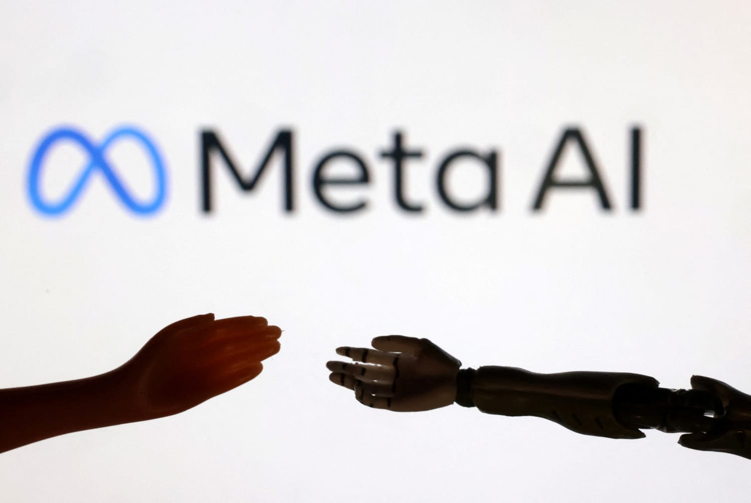 شعار Meta AI وخلفه يد بشرية وأخرى آلية. (رويترز)