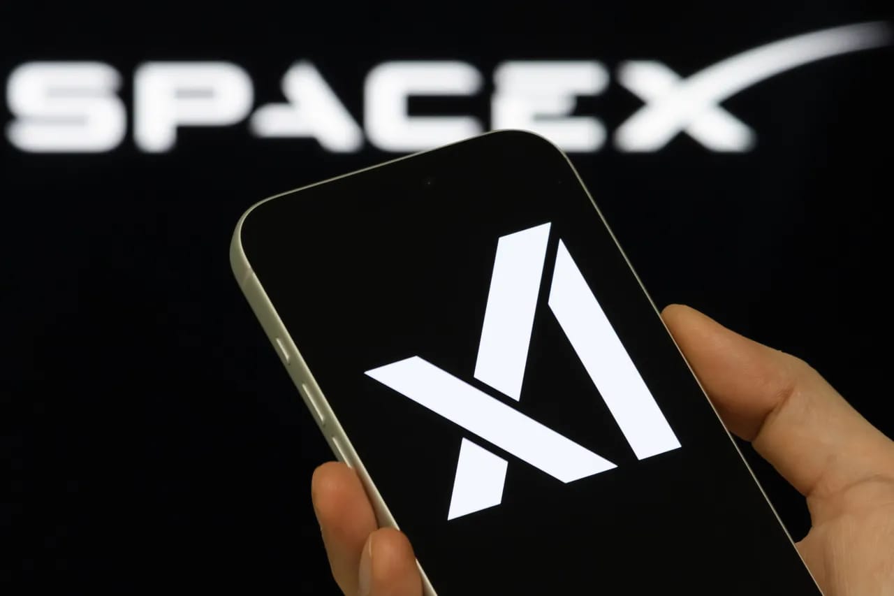 شعار شركة إكس إيه آي (xAI) على شاشة هاتف ذكي، مع ظهور شعار سبيس إكس (SpaceX) في الخلفية