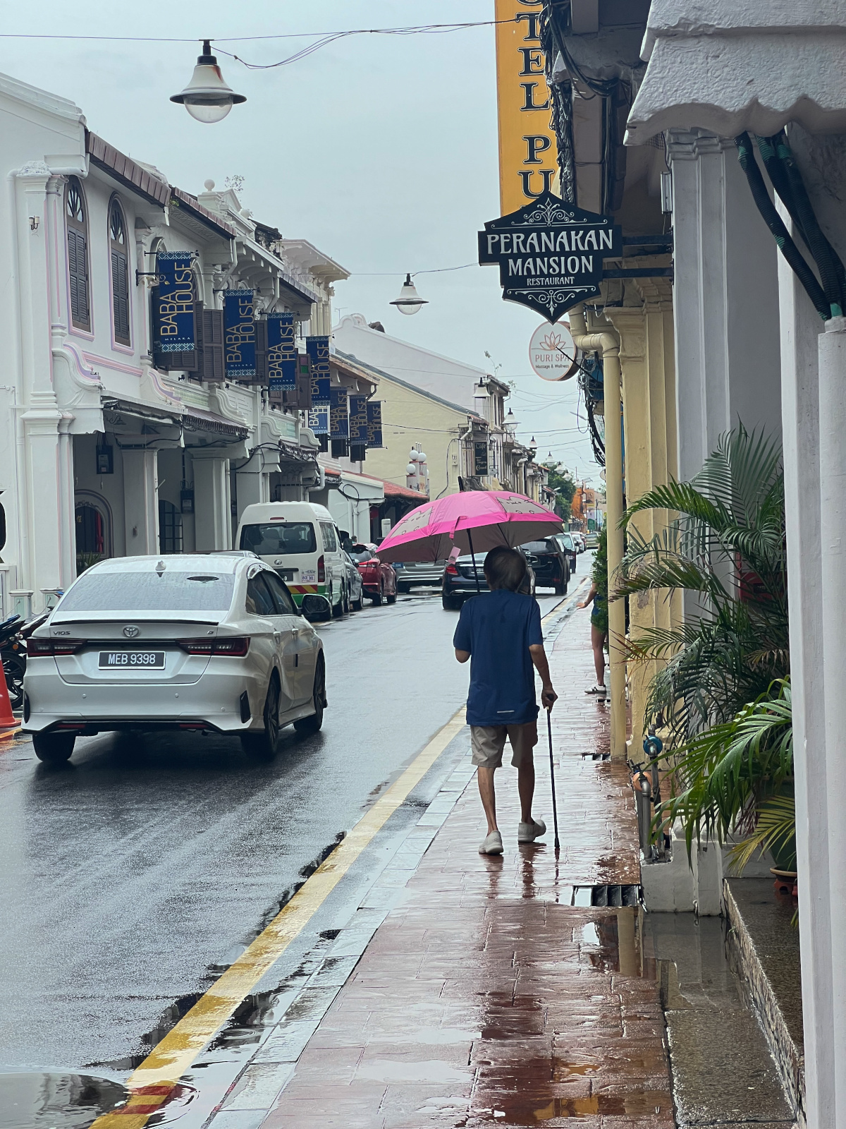 شارع ضيق من أحياء ملقا التاريخية بعد زخات المطر حيث تتجاور بيوت البيراناكان القديمة مع الحياة اليومية للمدينة (النهار)