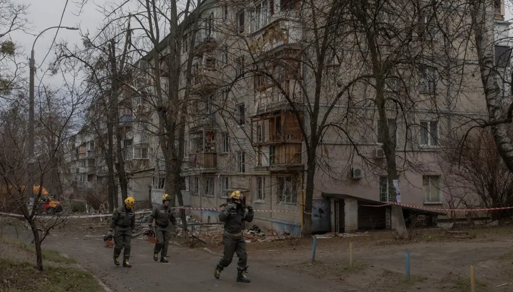 رجال الإنقاذ الأوكرانيون يسيرون بجوار مبنى سكني تعرض لأضرار بالغة في كييف. (أ ف ب)
