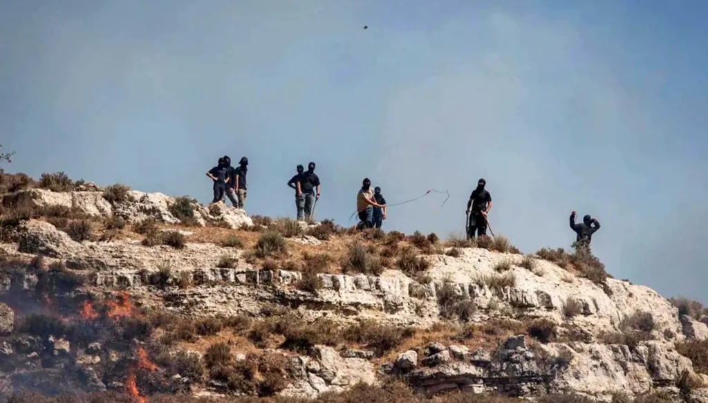 مستوطنون إسرائيليون ملثّمون يرشقون الفلسطينيين بالحجارة (أ ف ب)