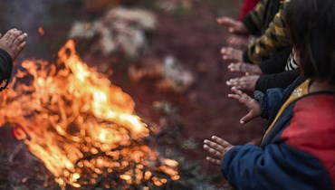 أطفال سوريون فرّوا من ريف محافظة حماة قبل أربع سنوات حول مدفأة من أغصان الزيتون (أ ف ب).