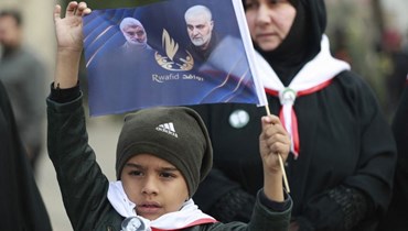 طفل عراقي يرفع صورة لسليماني والمهندس في بغداد (أ ف ب).