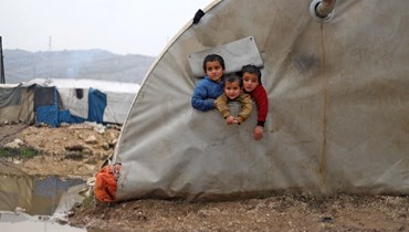 أطفال سوريون ينظرون من خيمتهم في مخيم البليع للنازحين قرب جسر الشغور في محافظة إدلب شمال غرب سوريا (13 ك2 2022، أ ف ب). 