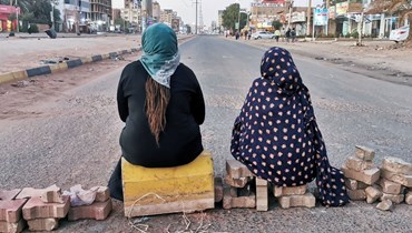 امرأتان سودانيتان جلستا عند حاجز اقفل شارع الستين بالعاصمة الخرطوم (18 ك2 2022، أ ف ب).