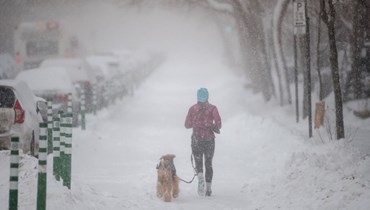 امرأة تهرول مع كلبها تحت الثلوج في مونتريال بكيبيك (17 ك2 2022، أ ف ب).