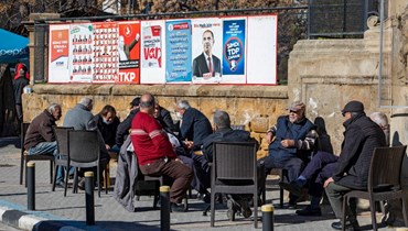 أشخاص جلسوا في مقهى بجوار ملصقات انتخابية في الجزء الشمالي من العاصمة القبرصية المقسمة نيقوسيا في جمهورية شمال قبرص التركية (20 ك2 2022، أ ف ب). 