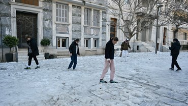 أشخاص يحاولون المشي في منطقة مغطاة بالجليد في وسط أثينا (26 ك2 2022، أ ف ب). 