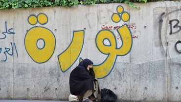 امرأة تجلس على حجر أمام حائط كتب غليه "ثورة" (حسام شبارو). 