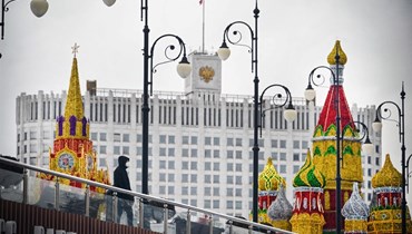 رجل يقف بجوار نموذج طبق الأصل لكاتدرائية القديس باسيل وبرج سباسكايا في الكرملين، قبالة مبنى الحكومة الروسية في وسط موسكو (8 شباط 2022، ا ف ب). 