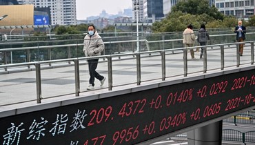 أشخاص يعبرون جسرا في الحي المالي بشنغهاي رفعت عليه لوحة مؤشرات تظهر أسعار الأسهم (22 شباط 2022، أ ف ب). 