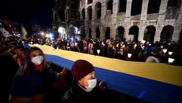 متظاهر يحمل علمًا أوكرانيا كبيرا أمام الكولوسيوم القديم خلال مسيرة في روما ضد الغزو الروسي لأوكرانيا (25 شباط 2022، أ ف ب). 