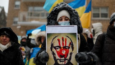 امرأة تحمل صورة لبوتين طبعت عليها يد ملطخة بالدم، خلال احتجاج للرعايا الأوكرانيين أمام القنصلية العامة لروسيا في مونتريال بكيبيك (25 شباط 2022، ا ف ب). 