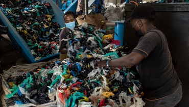 عاملان يجمعان نفايات من ورق البلاستيك في مصنع إعادة تدوير في نيروبي (26 شباط 2022، أ ف ب). 