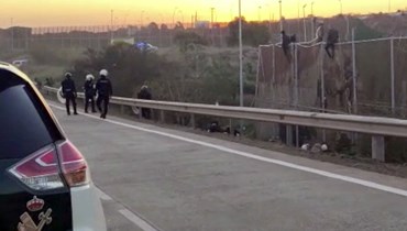 عناصر من الشرطة الإسبانية يراقبون مهاجرين وهم يتسلقون السياج الحدودي الفاصل بين جيب مليلية الإسباني والمغرب (3 آذار 2022، أ ف ب). 