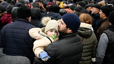 رجل يحمل طفله بينما تنتظر عائلات فرت من أوكرانيا دخول مخيم للاجئين في العاصمة المولدوفية شيسيناو (3 آذار 2022، أ ف ب). 