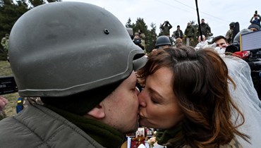 الجنديان في الدفاع الإقليمي الأوكراني فاليري (الى اليسار) وليسيا  يتبادلان القبلات خلال زواجهما على مقربة من نقطة تفتيش في ضواحي كييف (6 آذار 2022، أ ف ب). 