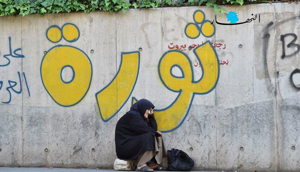 امرأة تجلس على حجر أمام حائط كتب غليه "ثورة" (حسام شبارو).