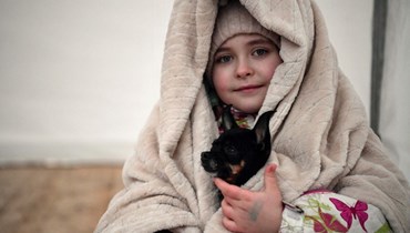 طفلة مع كلبها تنتظر نقلها في خيمة المنظمة الدولية للهجرة بعد عبور الحدود الأوكرانية البولندية (أ ف ب). 