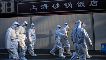 عمال بملابس واقية يعملون في منطقة في شنغهاي وضعت فيها حواجز لإغلاق الشوارع بعد اكتشاف اصابات جديدة بكورونا (15 آذار 2022، أ ف ب). 