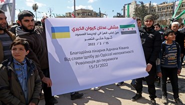 سوريون في مدينة إدلب يحملون لافتة تعلن التضامن مع أوكرانيا خلال إحياء الذكرى الـ11 للإنتفاضة ضد النظام السوري (أ ف ب).