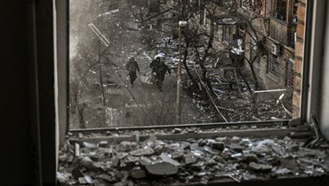 جنود أوكرانيون يشاهدون من نافذة مبنى وهم يحملون بقايا صاروخ بعد قصف منطقة سكنية في كييف (18 آذار 2022، أ ف ب).