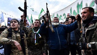 أشخاص يرفعون بنادقهم ويلوحون بأعلام المعارضة السورية في قرية الجنديريس في منطقة عفرين شمال حلب، خلال مسيرة في الذكرى الـ11 للانتفاضة ضد النظام (18 آذار 2022، أ ف ب). 